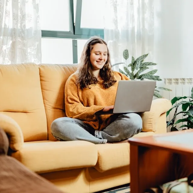 Smilding woman sitting on her couch with a laptop.